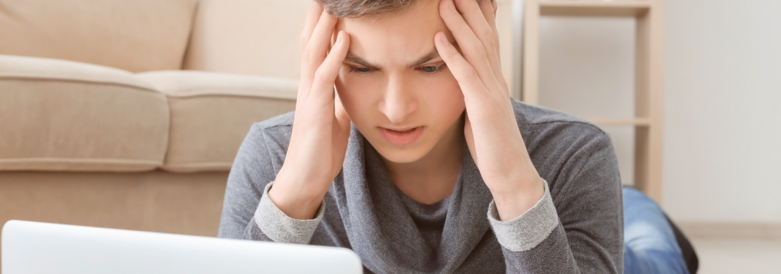 Abbildung ein Junge sitzt vor seinem Laptop und lässt sich mit beiden Händen an die Schlefe.